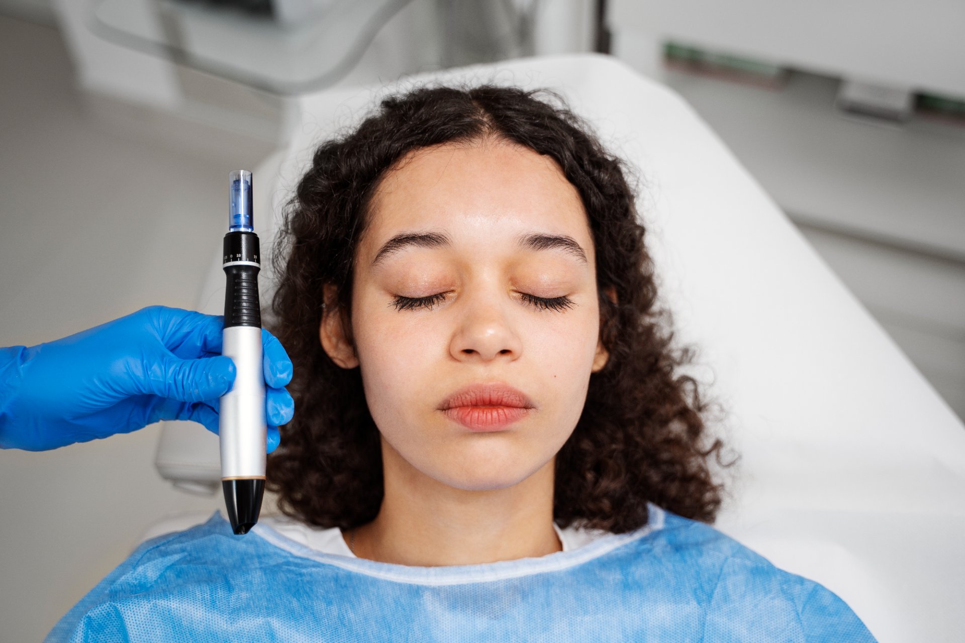 Pacientă pregătită pentru microneedling cu PRF, cu dispozitivul Dermapen ținut de medic lângă față